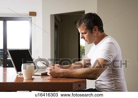 Stock Image - Man Reading Newspaper with Laptop and Coffee. Fotosearch