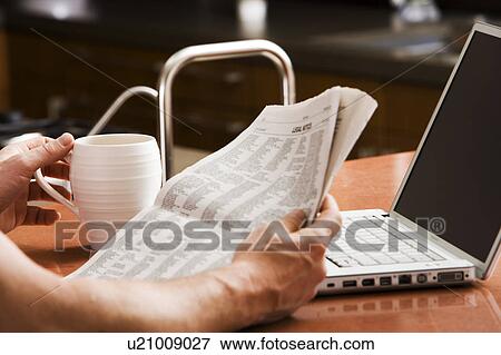 Stock Photo - Man Reading Newspaper with Laptop and Coffee. Fotosearch
