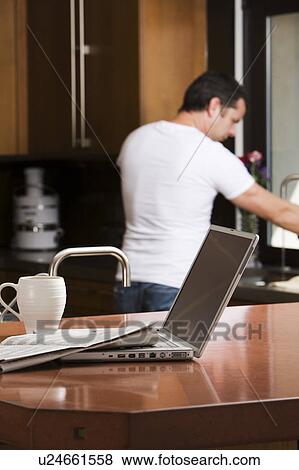 Man working in kitchen by laptop View Large Photo Image Stock Photo - Man working in kitchen by laptop. Fotosearch