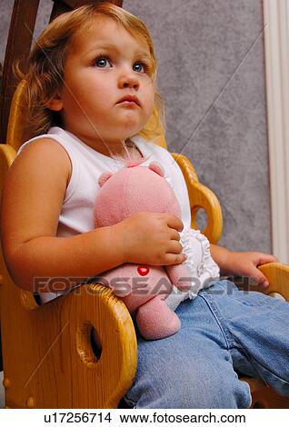 Picture - Close-up of a girl sitting in a chair and holding a stuffed toy. Fotosearch