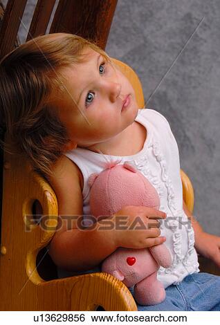 Stock Photograph - Close-up of a girl sitting in a chair and holding a stuffed toy. Fotosearch