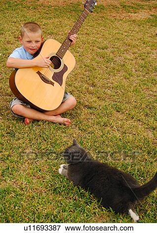 Boy playing a guitar with a cat sitting in front of him View Large Photo Image Stock Photo - Boy playing a guitar with a cat sitting in front of him. Fotosearch