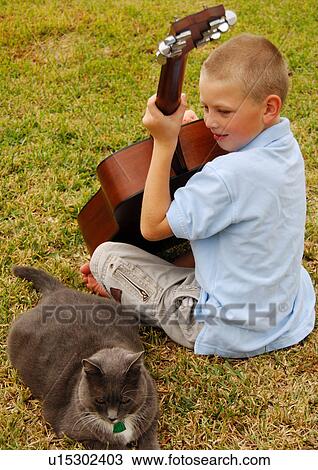 Rear view of a boy playing a guitar with a cat sitting beside him View Large Photo Image Stock Image - Rear view of a boy playing a guitar with a cat sitting beside him. Fotosearch