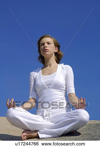 Low angle view of a young woman practicing yoga in the lotus position View Large Photo Image Stock Photograph - Low angle view of a young woman practicing yoga in the lotus position. Fotosearch