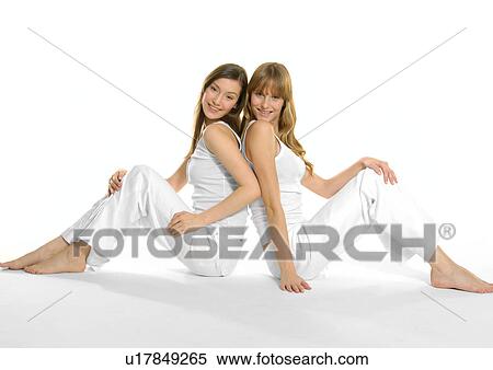 Stock Photography - Side profile of two young women sitting back to back and smiling. Fotosearch