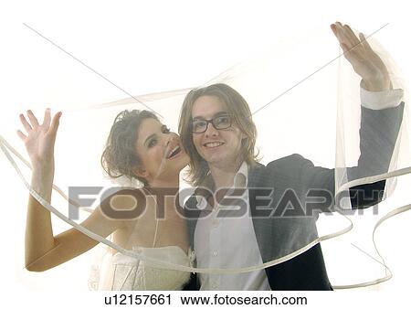 Stock Image - Portrait of a newlywed couple covering themselves with a veil. Fotosearch