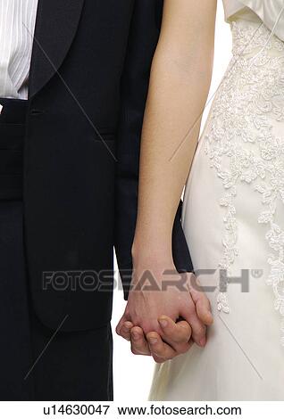 Stock Photo - Mid section view of a newlywed couple holding each other's hands. Fotosearch