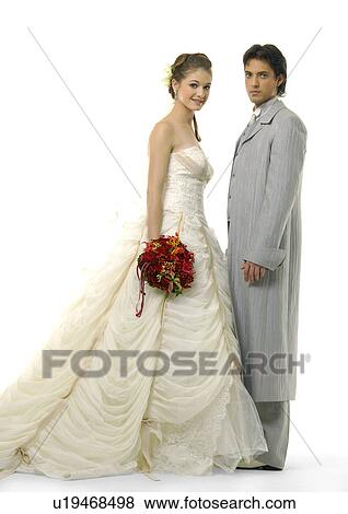 Portrait of a bride holding a bouquet of flowers with her groom standing in front of her View Large Photo Image Stock Photo - Portrait of a bride holding a bouquet of flowers with her groom standing in front of her. Fotosearch