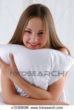 Stock Photograph - Close-up of a young woman hugging a pillow and smiling. Fotosearch