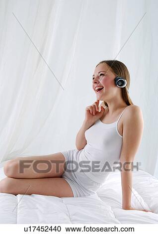 Young woman sitting on the bed and listening to music View Large Photo Image Stock Image - Young woman sitting on the bed and listening to music. Fotosearch