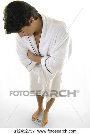 High angle view of a young man weighing himself on a scale View Large Photo Image Stock Photo - High angle view of a young man weighing himself on a scale. Fotosearch