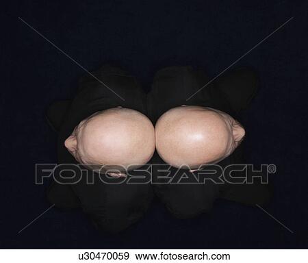 Stock Photo - Aerial view of bald identical twin men sitting back to back.. Fotosearch