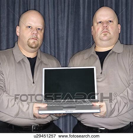 Bald identical twin men holding a laptop computer and looking at viewer. View Large Photo Image Stock Photo - Bald identical twin men holding a laptop computer and looking at viewer.. Fotosearch