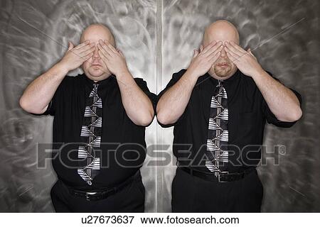 Stock Photo - Bald identical twin men standing with hands covering eyes. Fotosearch