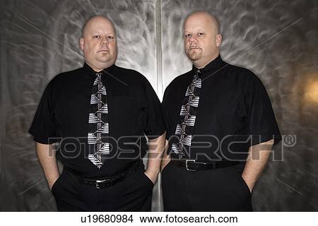 Bald mid adult identical twin standing together looking at viewer. View Large Photo Image Picture - Bald mid adult identical twin standing together looking at viewer.. Fotosearch