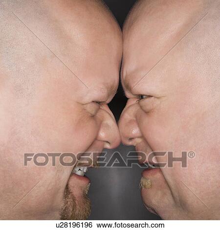 Stock Photograph - Close up of bald mid adult identical twin men standing face to face with angry expression.. Fotosearch