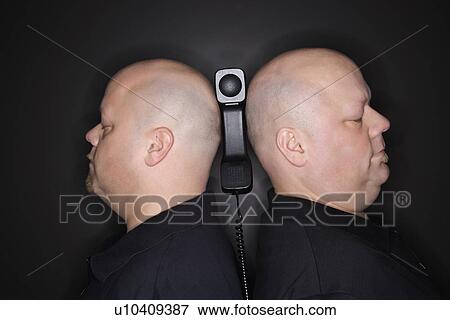 Stock Photo - Identical twin men standing back to back with telephone balancing between them.. Fotosearch