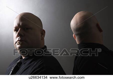 Picture - Mid adult bald identical twin men standing back to back and looking at viewer.. Fotosearch
