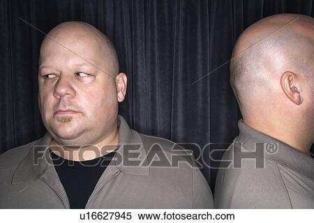 Stock Photography - Mid adult bald man looking away from his identical twin.. Fotosearch