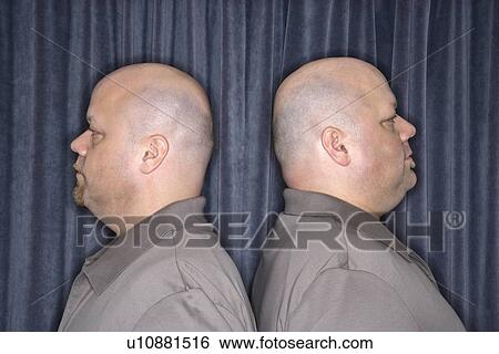 Stock Photograph - Profile of bald identical twin mid adult men standing back to back.. Fotosearch