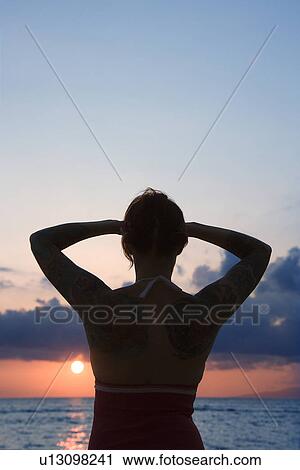 Stock Image - Attractive tattooed woman on beach at sunset . Fotosearch