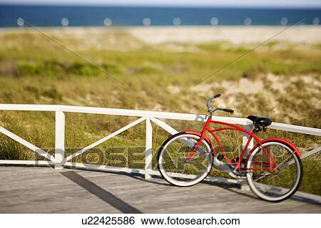 Stock Photograph - Red beach cruiser bicycle leaning against walkway rail on beach on Bald Head Island, North Carolina.. Fotosearch