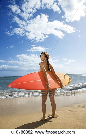 Stock Image - Young pretty woman in bikini standing with surfboard at beach . Fotosearch