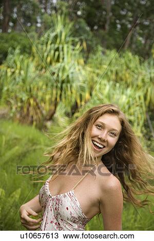 Stock Image - Beautiful happy Caucasian young adult woman in lush forest smiling and looking at viewer.. Fotosearch