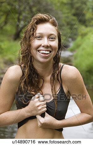 Stock Photograph - Wet Caucasian young adult woman standing in stream wringing water out of her shirt smiling and looking at viewer.. Fotosearch