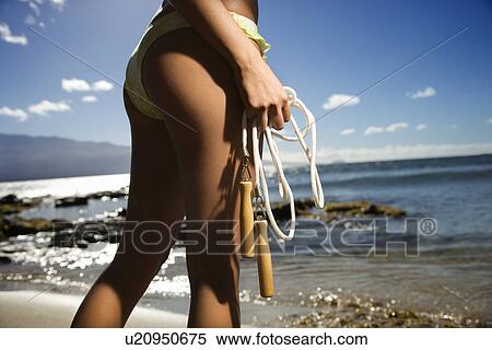 Female standing on beach in swimsuit holding jump rope View Large Photo Image Stock Photography - Female standing on beach in swimsuit holding jump rope. Fotosearch