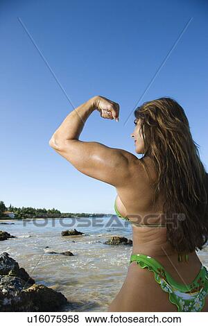 Stock Photo - Pretty Caucasian mid adult woman bodybuilder in bikini flexing bicep on beach.. Fotosearch