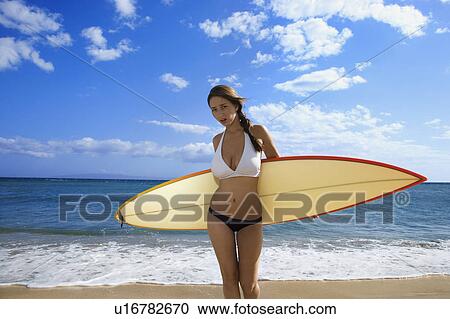 Stock Image - Young pretty Caucasian woman in bikini standing with surfboard at beach . Fotosearch