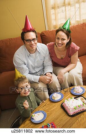 Stock Image - Boy and parents in party hats eating birthday cake. Fotosearch