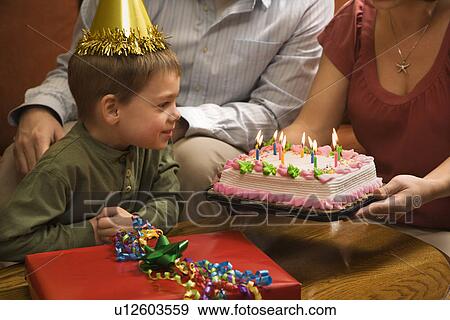 Stock Photo - Boy in party hat with Birthday cake and family. Fotosearch