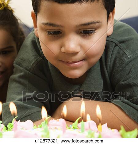 Stock Image - Boy looking down wishfully at lit candles of birthday cake with girl peeking in over his shoulder. Fotosearch