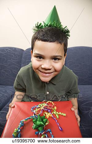 Boy wearing party hat holding large birthday present smiling and looking at viewer View Large Photo Image Stock Image - Boy wearing party hat holding large birthday present smiling and looking at viewer. Fotosearch
