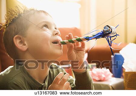 Stock Image - Caucasian boy at birthday party blowing noisemaker.. Fotosearch