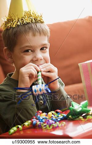Stock Photography - Caucasian boy at birthday party looking at viewer blowing noisemaker.. Fotosearch
