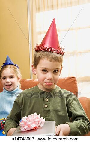 Stock Image - Caucasian boy wearing party hat pouting and looking at viewer.. Fotosearch