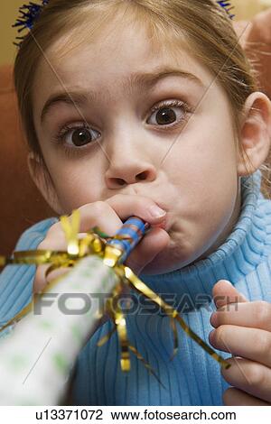 Stock Image - Caucasian girl blowing noisemaker and making facial expression.. Fotosearch