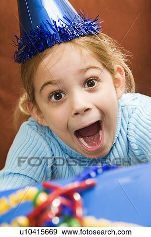 Stock Photo - Caucasian girl wearing party hat holding gift and looking at viewer with excited expression.. Fotosearch