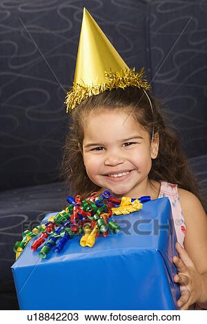 Girl wearing party hat holding birthday present smiling and looking at viewer View Large Photo Image Stock Image - Girl wearing party hat holding birthday present smiling and looking at viewer. Fotosearch