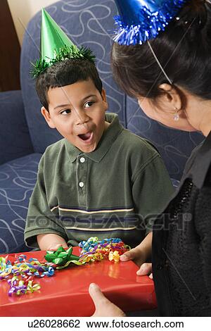 Stock Image - Mother giving present to surprised son at birthday party. Fotosearch