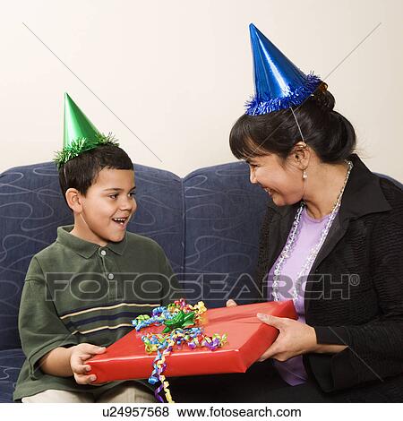 Stock Photo - Mother giving present to surprised son at birthday party. Fotosearch