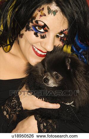 Stock Photograph - Smiling Caucasian woman in unique makeup holding black Pomeranian dog.. Fotosearch