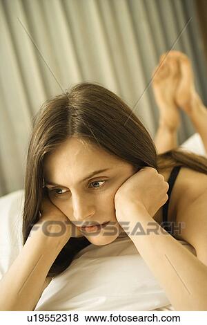 Stock Photo - Caucasian mid-adult woman lying on bed with head on hands.. Fotosearch