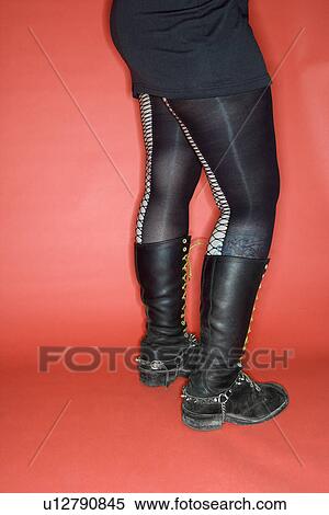 Stock Photography - Portrait of woman's lower body wearing leggings and boots against orange background. Fotosearch
