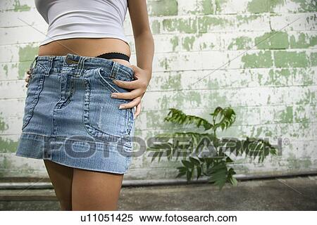 Stock Photography - Torso shot of mid-adult blonde woman wearing blue jean mini skirt with underwear showing beside building in alley. Fotosearch