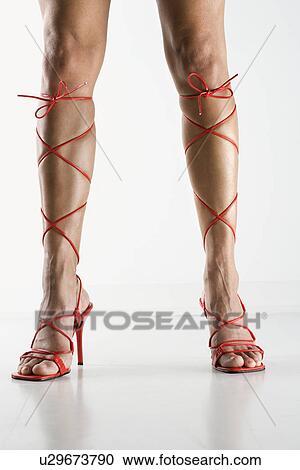 Stock Image - Woman's legs and feet wearing sexy red high heel shoes that lace up to her knees.. Fotosearch