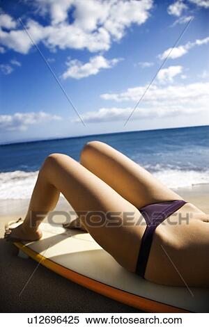Stock Photography - Young woman in bikini lying on surfboard sunbathing at beach . Fotosearch
